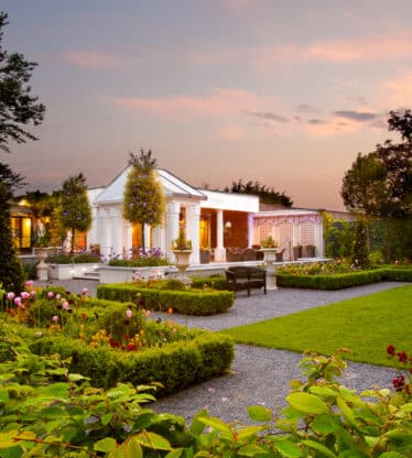 Elegant hotel gardens at sunset with gazebo, lush greenery, vibrant flowers, and inviting patios.