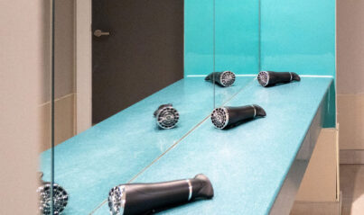 Modern hotel bathroom with dryers, turquoise accents, and sleek mirrors enhancing guest convenience and style.