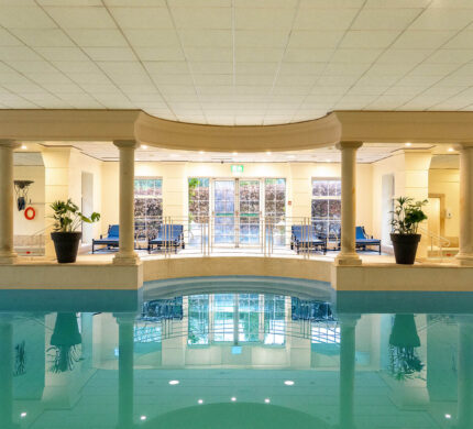 Elegant indoor pool area with loungers and lush plants at luxury hotel, perfect for relaxation and rejuvenation.