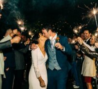 Guests enjoy a joyful outdoor wedding celebration with sparklers, featuring elegant evening attire and vibrant smiles.