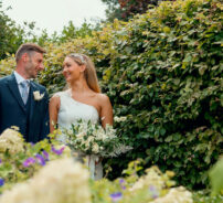 A joyful couple poses in lush garden with vibrant flowers, offering a romantic backdrop for weddings at our boutique hotel.