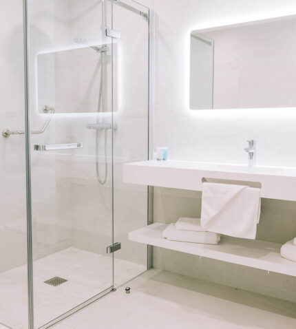 Elegant hotel bathroom with glass-enclosed shower, illuminated mirror, and modern fixtures, offering a relaxing stay.