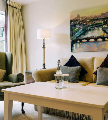 Elegant hotel lounge with plush seating, cityscape art, garden views, and complimentary refreshments.