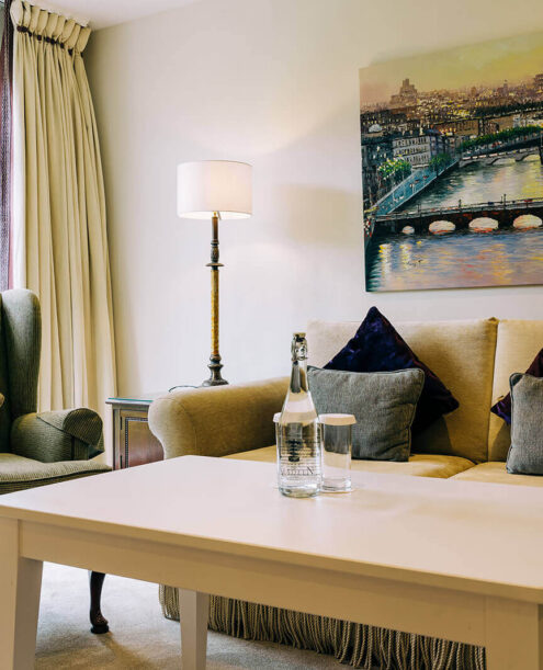 Elegant hotel lounge with plush seating, cityscape art, garden views, and complimentary refreshments.