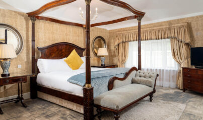 Luxurious hotel room with opulent four-poster bed, cosy chaise longue, elegant decor, and wall-mounted flat screen TV.