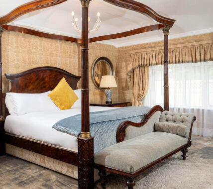 Luxurious hotel room with opulent four-poster bed, cosy chaise longue, elegant decor, and wall-mounted flat screen TV.
