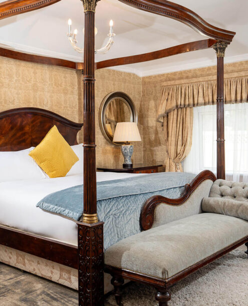 Luxurious hotel room with opulent four-poster bed, cosy chaise longue, elegant decor, and wall-mounted flat screen TV.