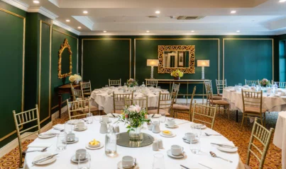 Elegant banquet hall with round tables set for dining, featuring gold-accented mirrors and floral centrepieces, perfect for events.