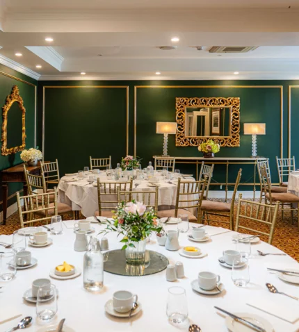 Elegant banquet hall with round tables set for dining, featuring gold-accented mirrors and floral centrepieces, perfect for events.